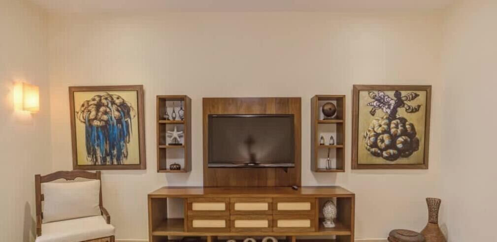 Un salon équipé d’un téléviseur, d’un meuble de rangement en bois et décoré d’œuvres d’art sur les murs.