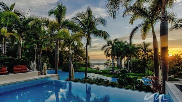 A swimming pool with palm trees and a sunset view. - 3BR beach condo - pool, shore access & bay views (Cruz de Huanacaxtle)
