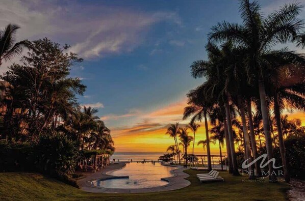 A resort with a pool, palm trees, and a sunset view.