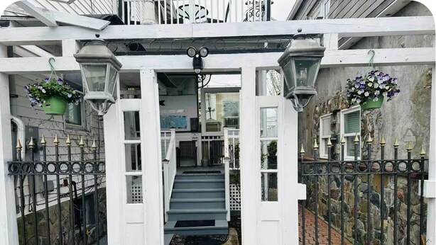 Un edificio blanco con una escalera central, rejas de metal negro y macetas colgantes.