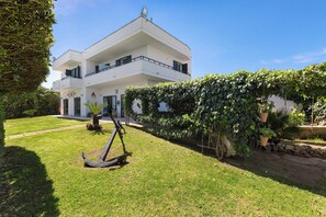 A modern two-story building with a flat roof, large windows, and a well-maintained garden with a sculpture.
