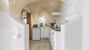 A narrow kitchen with white appliances, a stone archway, and a tiled floor. - La Casa delle Rondini by BarbarHouse (Torricella)