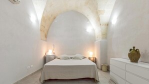 A bedroom with a large arched ceiling, a bed with a white bedspread, bedside lamps, a small bedside table, a nightstand, a dresser, and a vase on the dresser. - La Casa delle Rondini by BarbarHouse (Torricella)