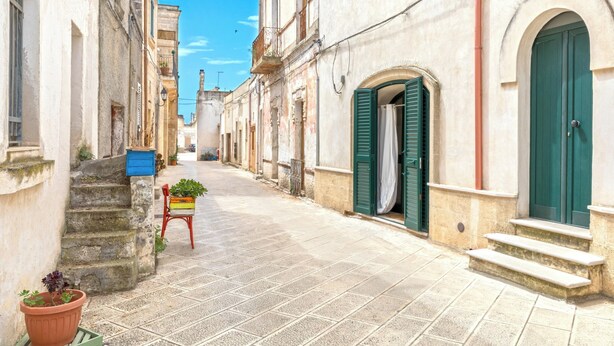 A narrow street with buildings on either side, stone steps, and a small chair with a plant. - La Casa delle Rondini by BarbarHouse (Torricella)