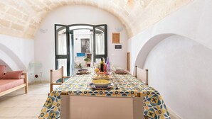 A dining area with a table set for a meal, a bed with a pink pillow, and a stone wall. - La Casa delle Rondini by BarbarHouse (Torricella)