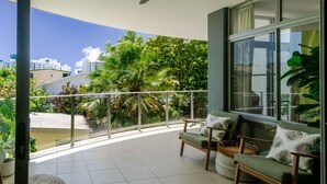 Un balcon doté d’un espace salon, offrant une vue sur la verdure et avec un bâtiment visible au loin.
