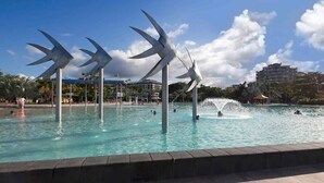 Une piscine avec trois grandes structures blanches, en forme de voiles, qui émergent de l’eau.