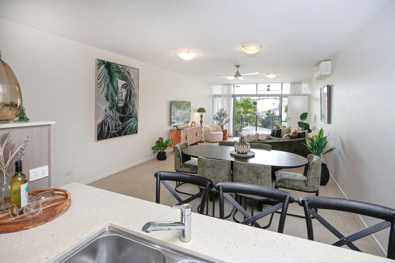 A modern kitchen with a dining area, large windows, and a ceiling fan.