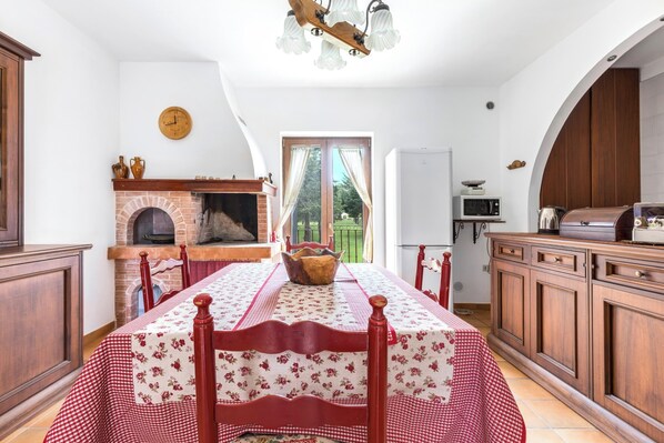 Un comedor con mantel a cuadros, un banco de madera, una chimenea de ladrillo y vistas al exterior a través de una ventana.