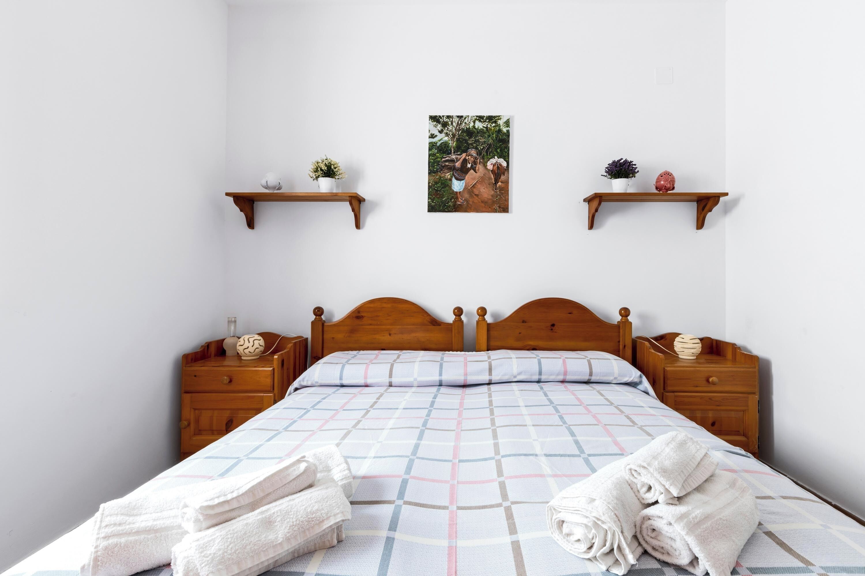 Un letto rifatto con una coperta a quadri, due comodini in legno con lampade e due mensole a parete con oggetti decorativi.