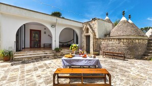 A courtyard with a table set for a meal, stone walls, and a small building with a conical roof.