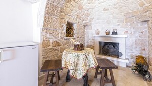 A stone-walled room with a fireplace, a table with a tablecloth, and a wine rack.