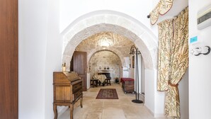 A hallway with an arched stone ceiling, a wooden piano, a fireplace, and a patterned curtain.