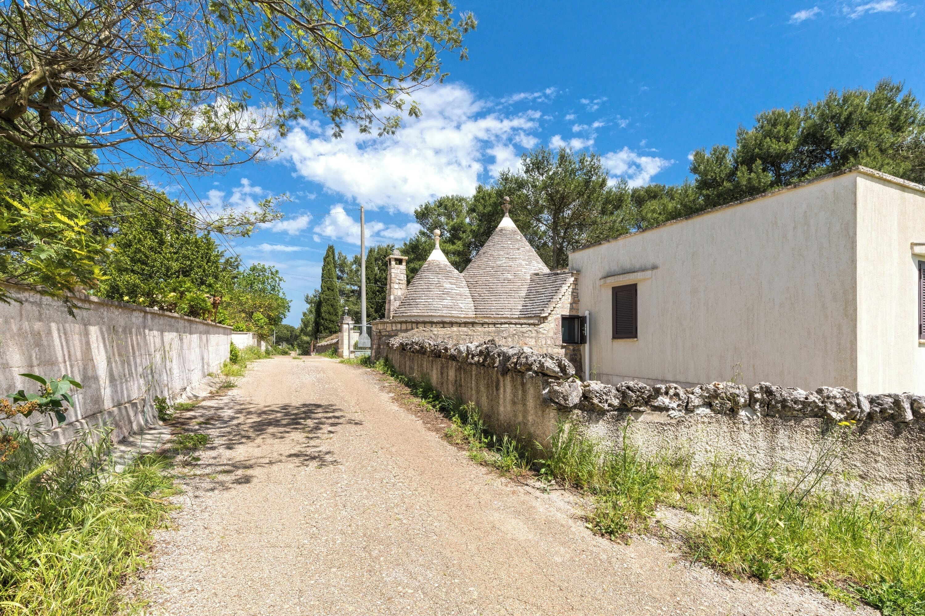 A narrow gravel path leading to a white building with a stone wall on one side and a stone roof.