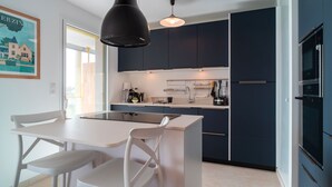 Une cuisine moderne avec des meubles bleu foncé, un îlot central blanc doté de sièges et un luminaire suspendu.