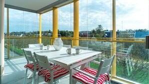 Un balcon avec une table et des chaises blanches, une balustrade en verre et une vue sur la ville.