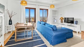 Een moderne woonkamer met een blauwe bank, een houten eettafel en een televisie.