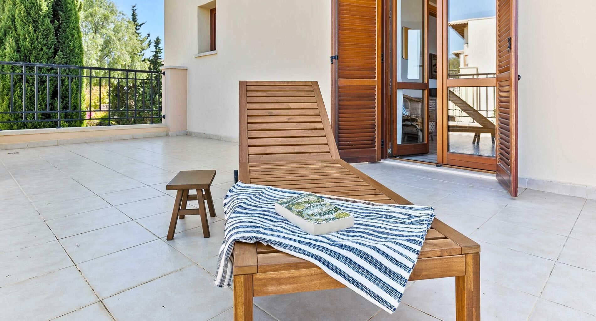 A sunbed with a striped blanket and a small wooden stool on a tiled patio.