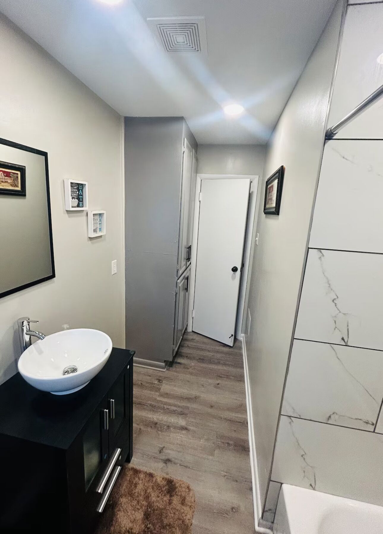 A modern bathroom with a white sink, black vanity, marble shower, and a door leading to another room.
