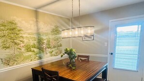 A dining area with a wooden table, chairs, a hanging light fixture, and a mural on the wall. - El Rancho Powell (Goldsboro)