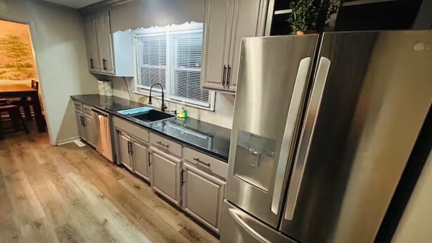 A modern kitchen with stainless steel appliances, wooden flooring, and a window with blinds. - El Rancho Powell (Goldsboro)
