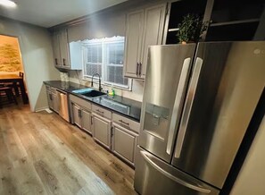 A modern kitchen with stainless steel appliances, wooden flooring, and a window with blinds. - El Rancho Powell (Goldsboro)