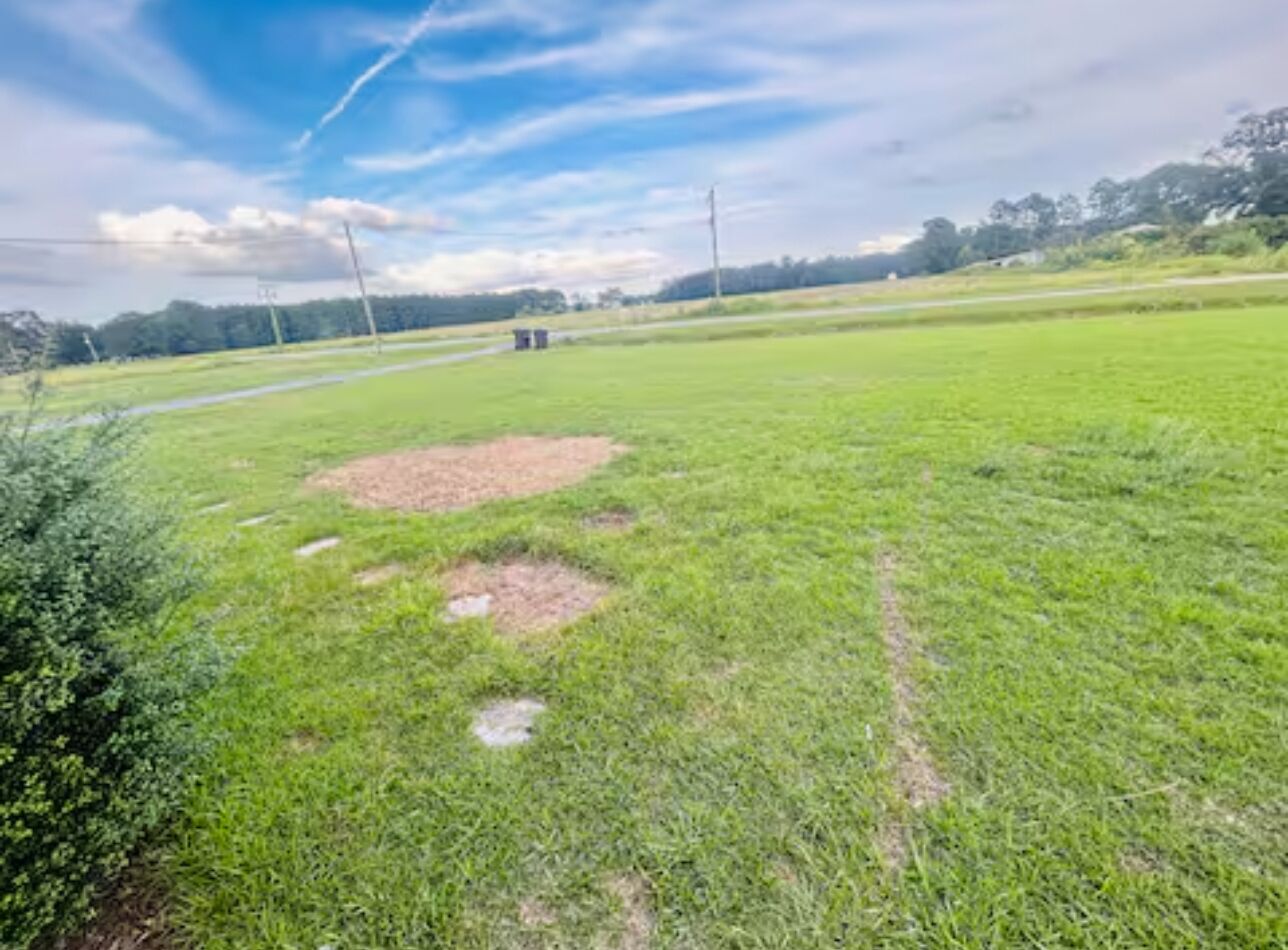 A grassy field with a dirt patch and a small structure in the distance.