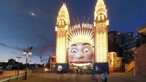 Una entrada grande e iluminada con el texto “LUNA PARK” y una llamativa decoración con rostro caricaturesco.