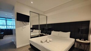 Una habitación de hotel moderna con una cama grande, un espejo, un televisor y una mesita auxiliar.