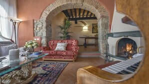 A cozy living room with a red sofa, a piano, a fireplace, and a stone archway. - My Rental Homes - Villa delle Rose with private pool, barbeque and air conditioning (Serravalle Pistoiese)