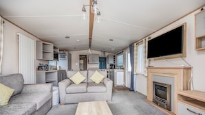 A compact living space with a sofa, coffee table, TV, fireplace, and kitchenette. - Charming Home in Lakeside Park - Pass The Keys (Chichester)