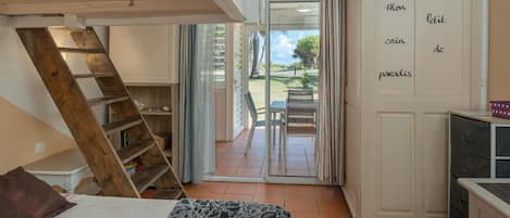 Un dormitorio con cama, una escalera de madera, un armario y una puerta corrediza de vidrio que da a un balcón.
