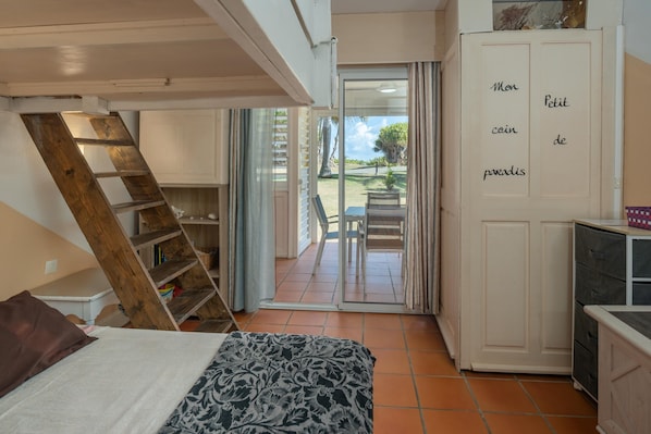 Une chambre à coucher comprenant un lit, une échelle en bois, une armoire et une porte-fenêtre coulissante donnant sur un balcon.