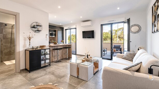 A modern living room with a sofa, coffee table, and a kitchen area with a bar. - Les Vagues d'Agosta - Studio Apartment, Sleeps 2 (Albitreccia)