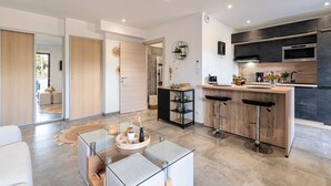 A modern kitchen with a central island, bar stools, and a dining area with a glass table. - Les Vagues d'Agosta - Studio Apartment, Sleeps 2 (Albitreccia)