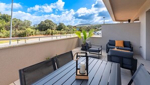 A balcony with a table, chairs, and a sofa. There is a view of the city and greenery in the background. - Les Vagues d'Agosta - Studio Apartment, Sleeps 2 (Albitreccia)