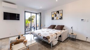 A modern bedroom with a bed, a TV, a glass table, and a view of the outdoors. - Les Vagues d'Agosta - Studio Apartment, Sleeps 2 (Albitreccia)