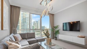 Una sala de estar moderna con un sofá modular, una mesa de centro de vidrio, un televisor en la pared y vistas de edificios altos.