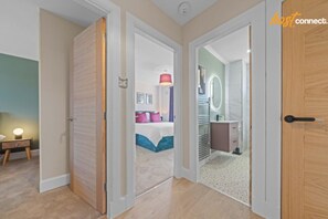 A hotel room with a bed, bedside table, and a bathroom with a mirror and sink. - Modern 2BR in Dunfermline | Sleeps 4 (Cairneyhill)