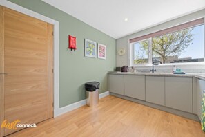 A kitchen with a wooden floor, a window with a view of trees, and a trash bin. - Modern 2BR in Dunfermline | Sleeps 4 (Cairneyhill)