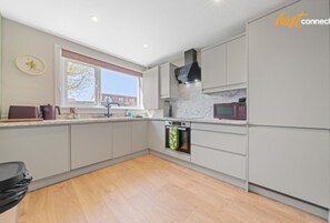 A modern kitchen with grey cabinets, a built-in oven, and a microwave. - Modern 2BR in Dunfermline | Sleeps 4 (Cairneyhill)