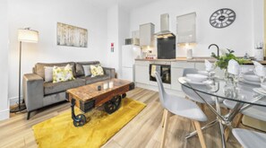 Ein modernes Wohnzimmer mit Sofa, Couchtisch und Essbereich mit Stühlen und einem Glastisch.