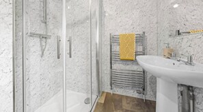 Une salle de bain avec une douche à parois de verre, un lavabo blanc et un porte-serviettes orné d’une serviette à motifs.