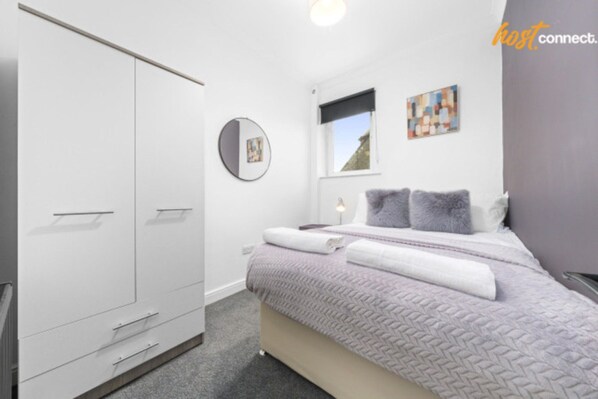 Un dormitorio moderno con una cama, un armario, un espejo redondo y una ventana con vistas.