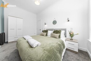Ein modernes Schlafzimmer mit einem großen Bett, einem Kleiderschrank, einem Nachttisch mit Lampe und einer kleinen Pflanze.