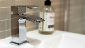 Een badkamer met een moderne kraan en een fles vloeibare zeep op het aanrecht.