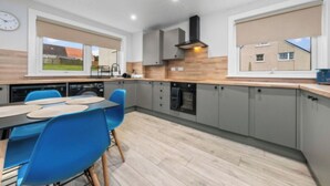 Een moderne keuken met grijze kastjes, een houten aanrecht en een eethoek met blauwe stoelen.