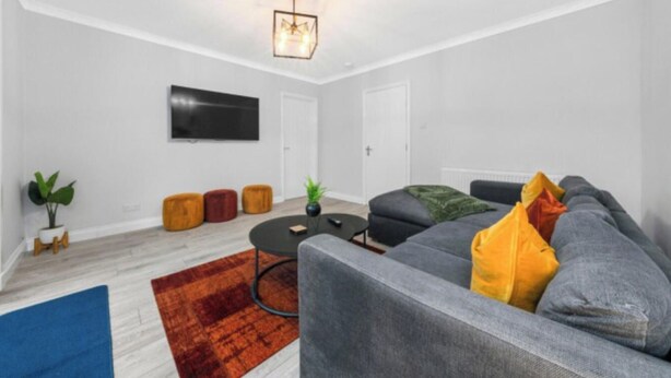 Een moderne woonkamer met een grijze bank, een salontafel en een flatscreen televisie aan de muur.