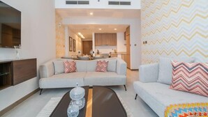 A modern living room with a sofa, a coffee table, and a TV. There is a kitchen in the background.