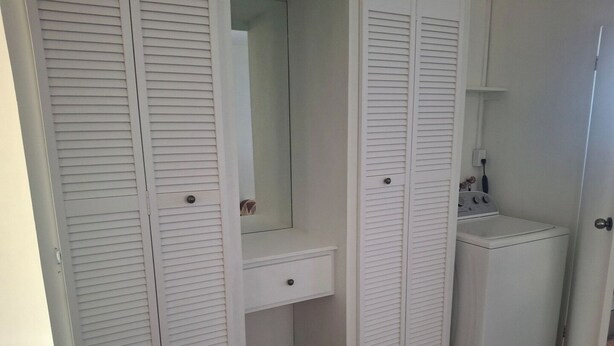 A small, enclosed walk-in closet with a built-in vanity, a washing machine, and a mirror. - Fair View Garden #2 (By-BLR) (Fair View)